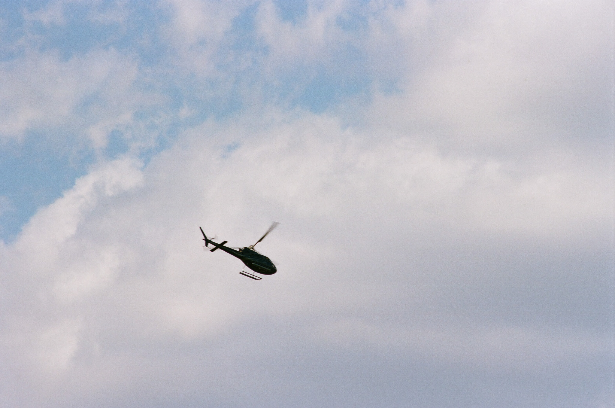 A helicopter flying against a sky of clouds.