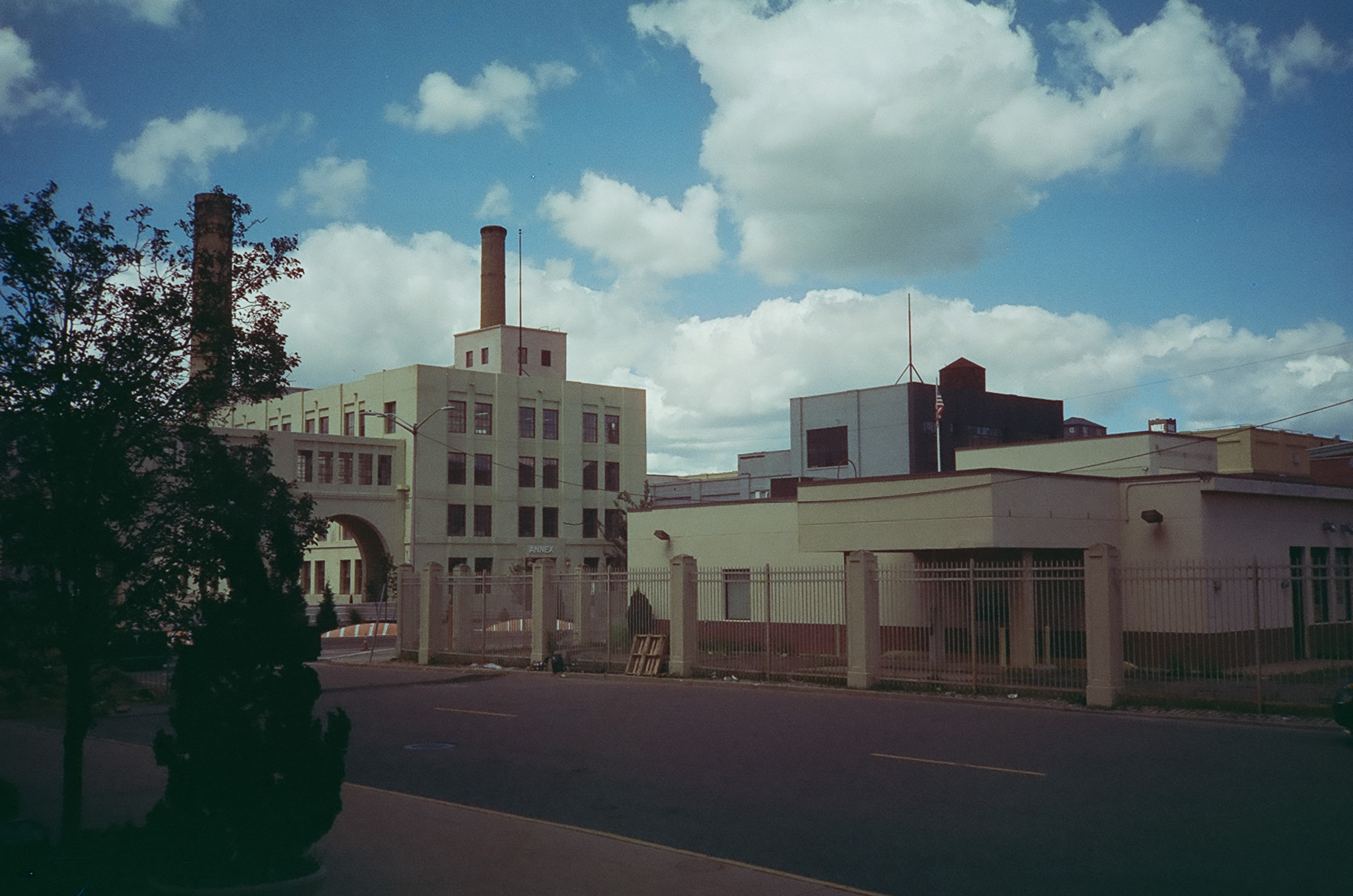 Several trees in front of some stucco industrial buildings on a cloudy day.