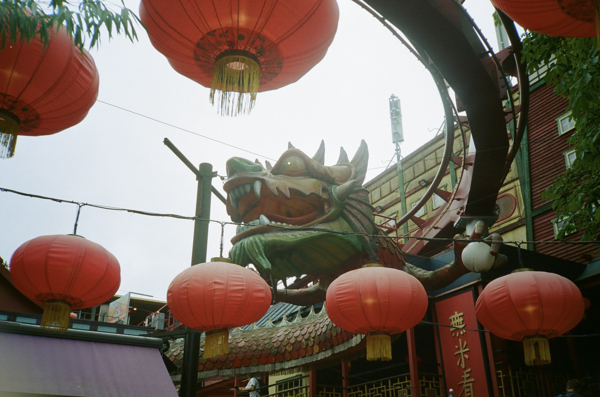 A Chinese dragon underneath the rail of a roller coaster. Several red Chinese lanterns hang on wires.