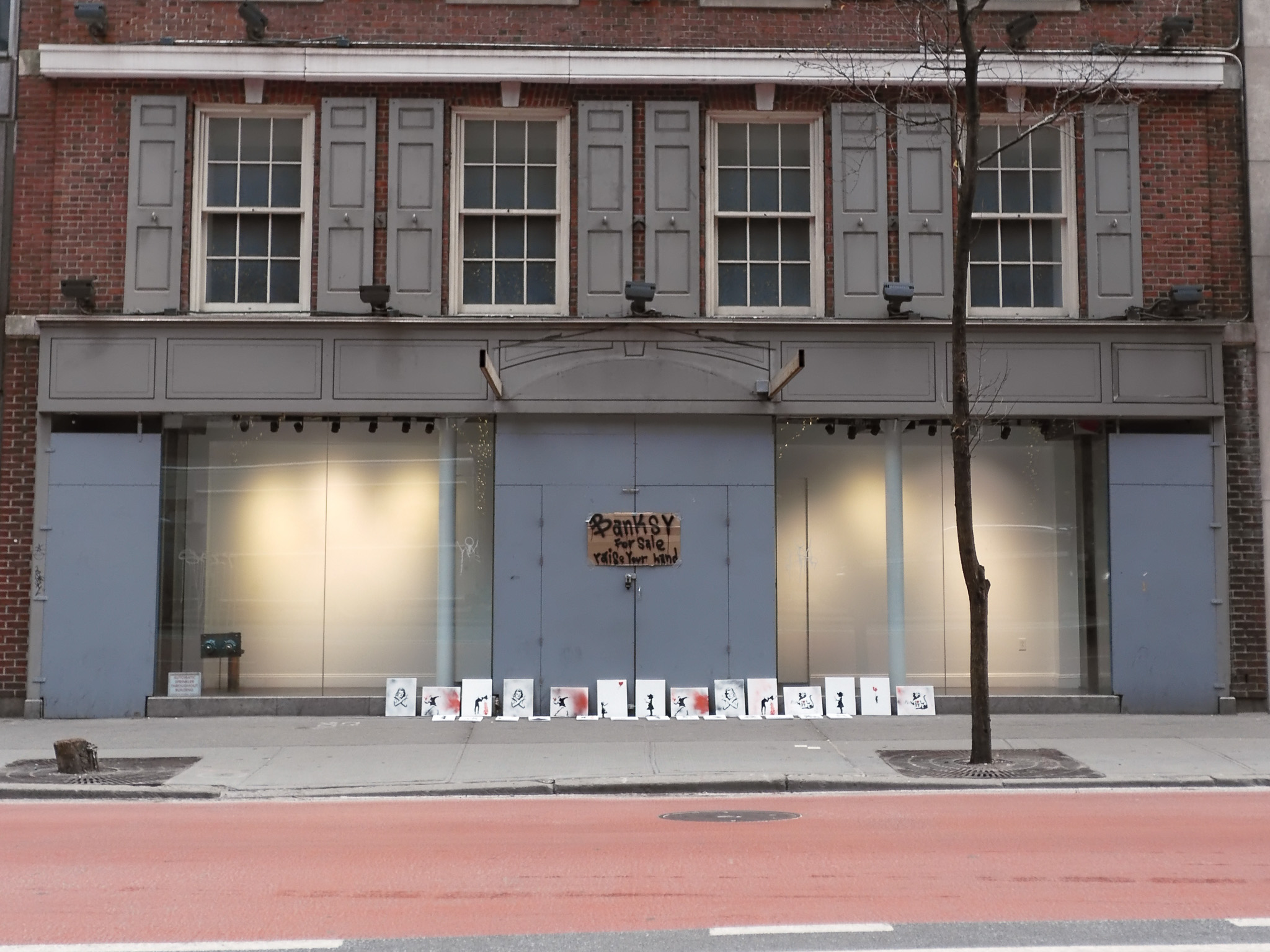 A bunch of canvas of Bankseys beneath a sign that says Banksay for sale raise your hand