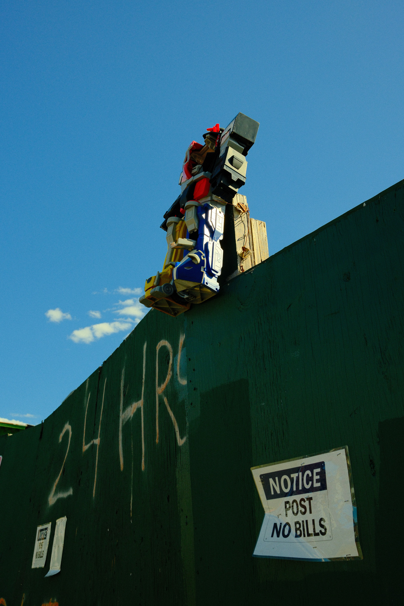 A Power Rangers Megazord toy tied to the top of construction fence post.