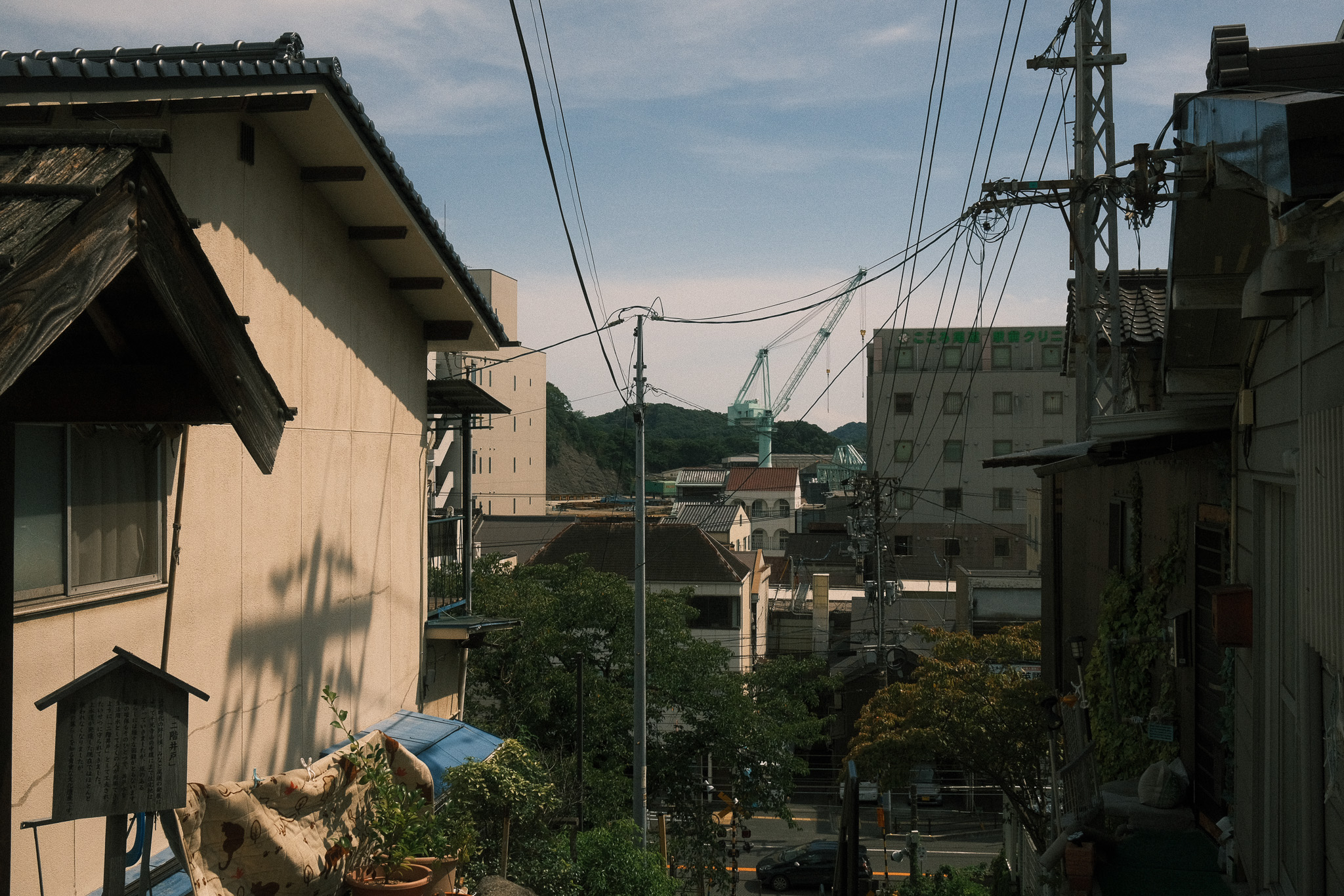 A small street between two rows of houses on a hill with a seafoam green crane in the distance.