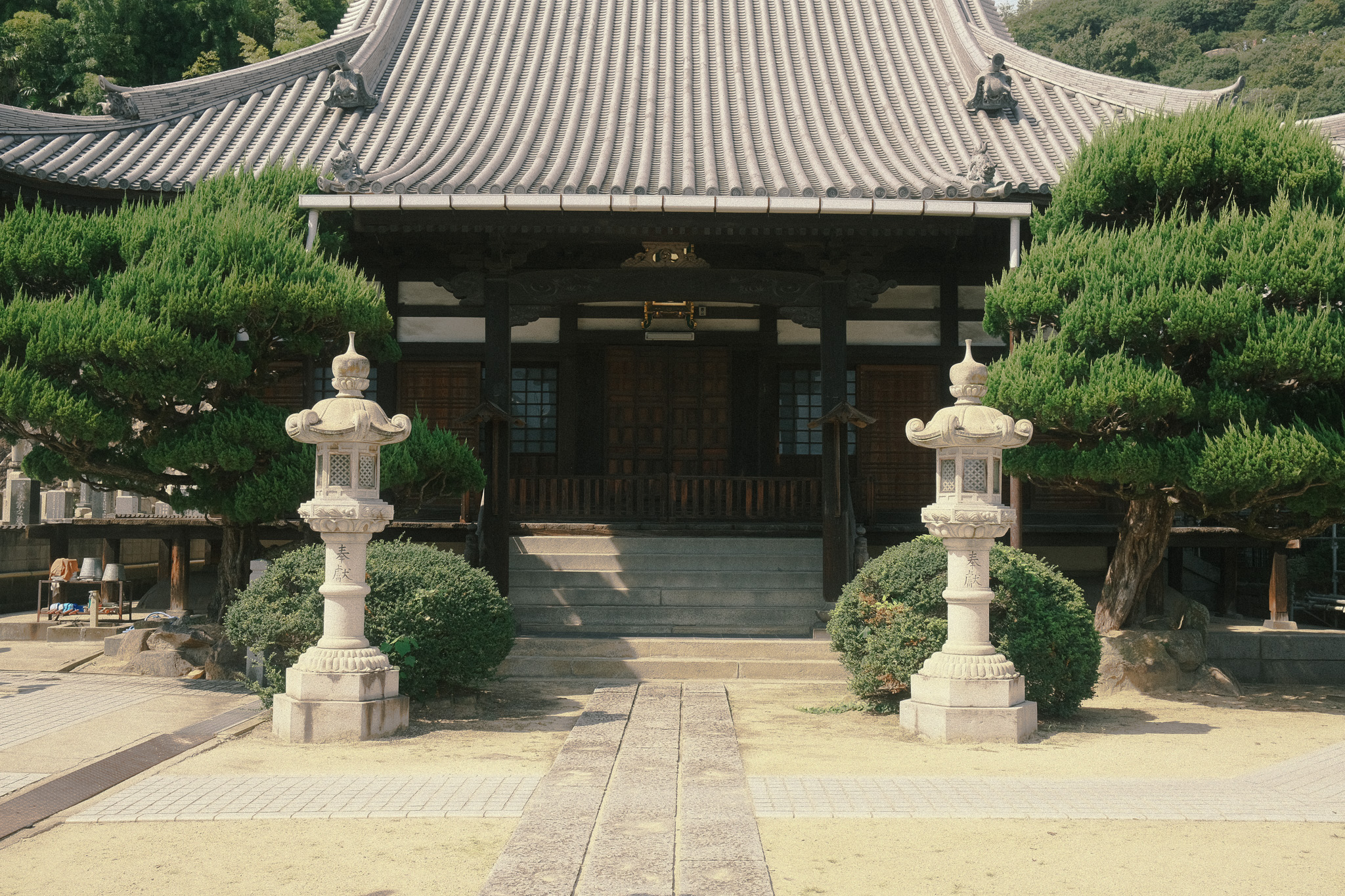 Shojozankomyo Temple. A Buddhist temple 's main door with two stone lanterns flanked by evergreen trees.