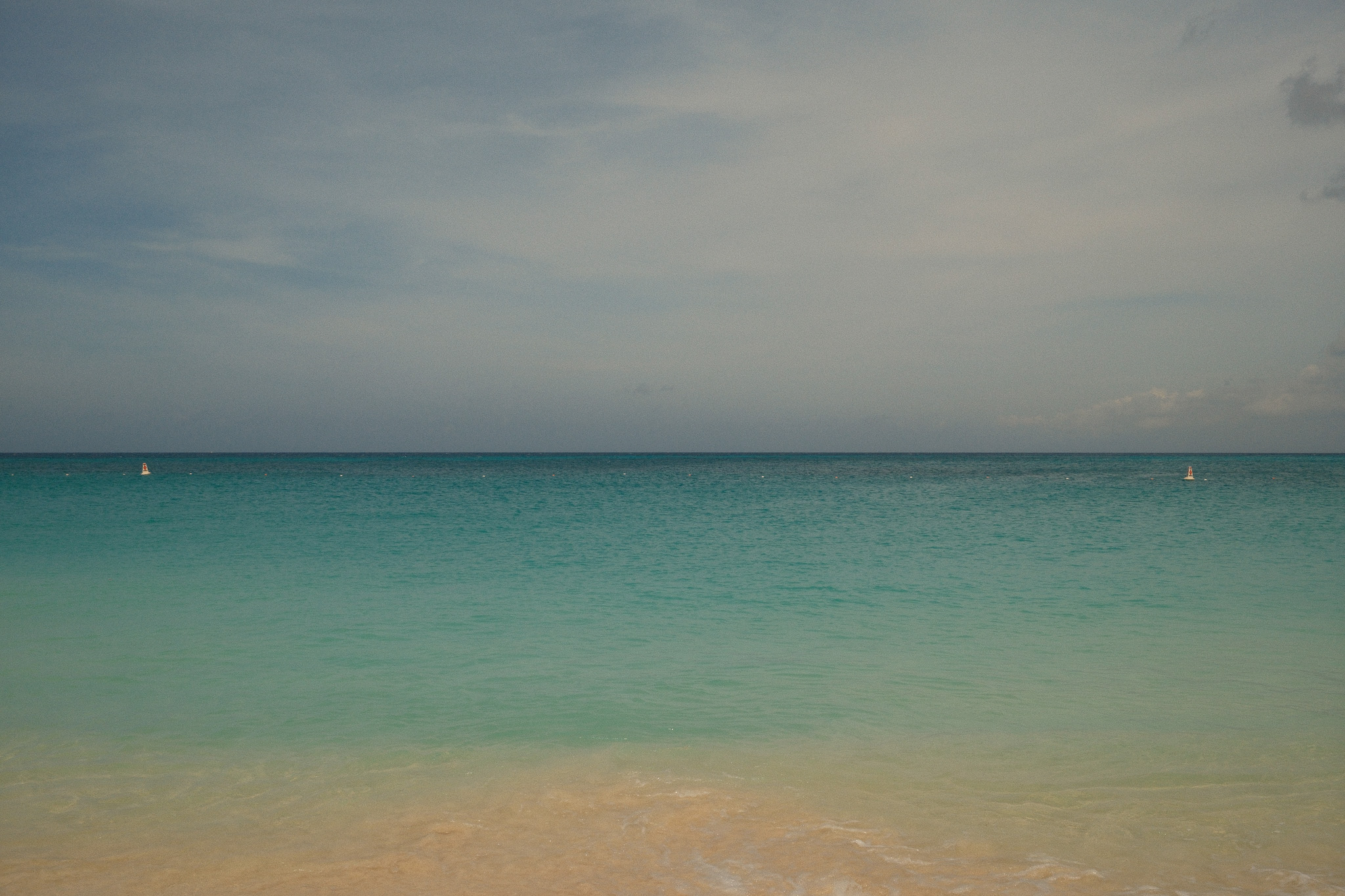 The beach and turquoise blue water of Aruba with two small buoys marking the safe area