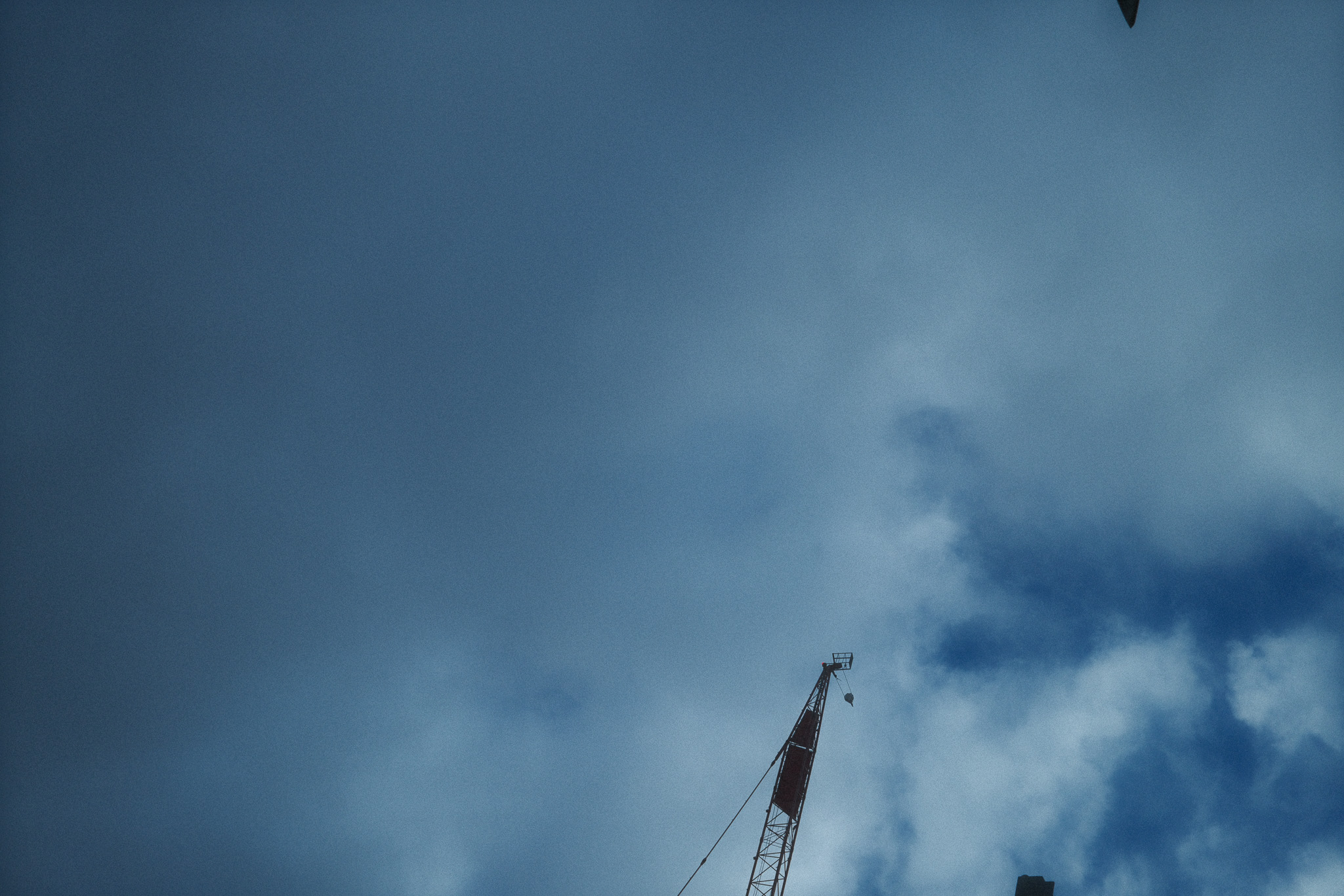 A cloudy grey sky seen through a few cranes looking up.