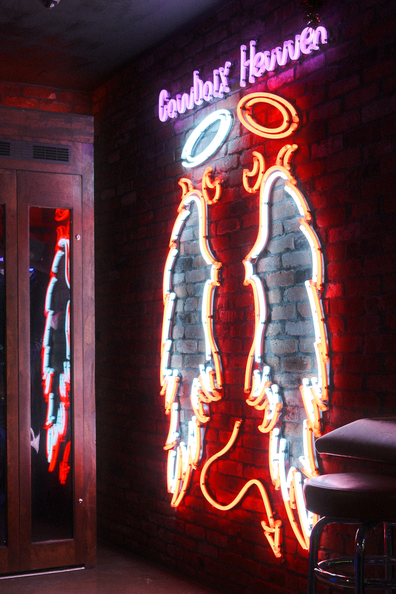 A neon wall hanging with angel wings, a devil tail, two halos, and the words Cowboix Hevvven