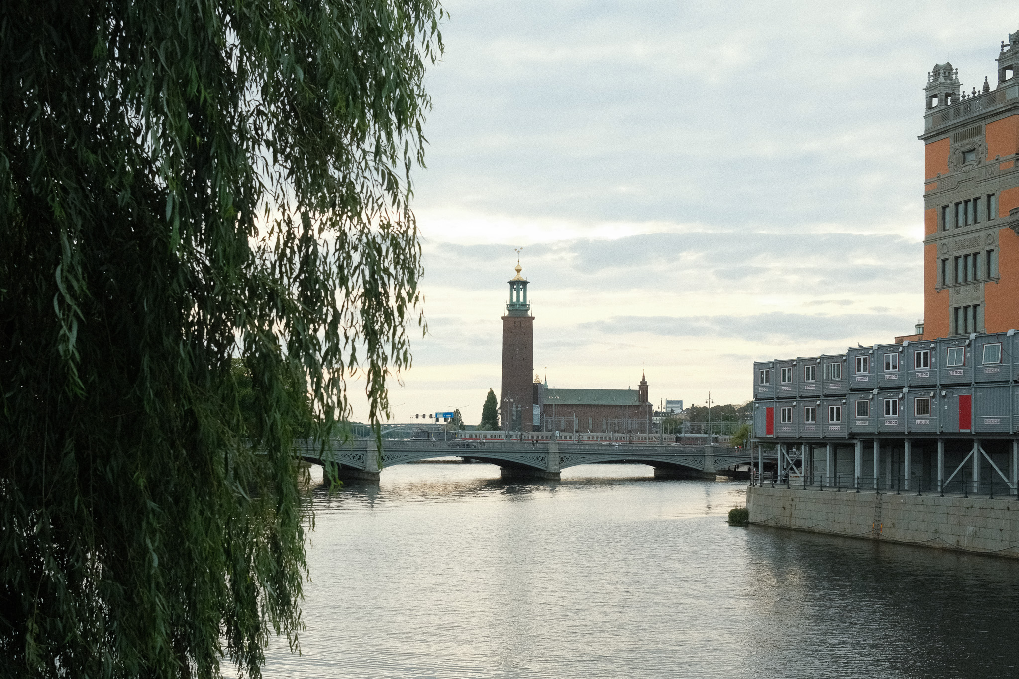 A large brick building with a copper roof on the waterfront behind a bridge.