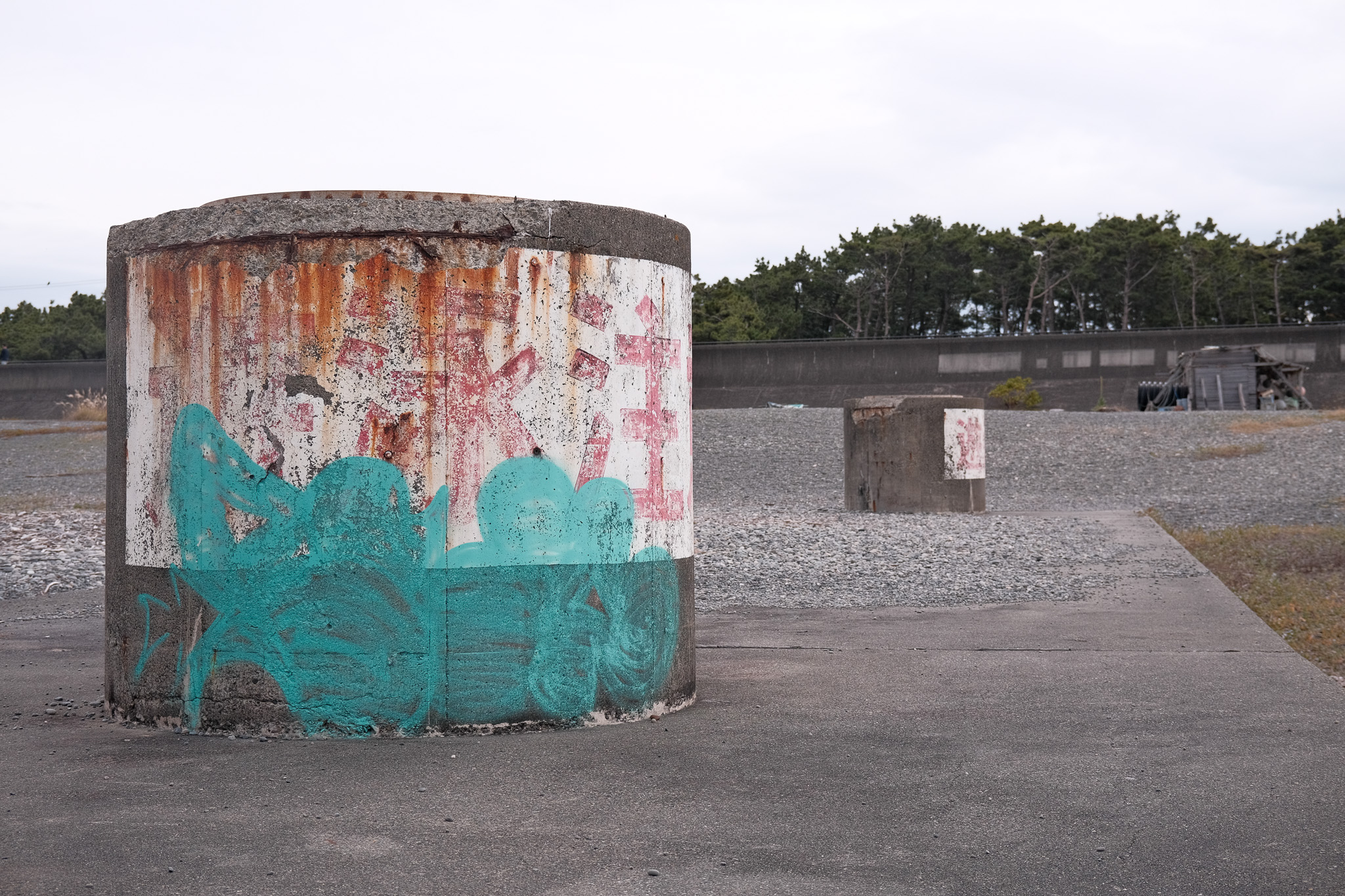 Worn out concrete storm drain outflow sewers on a rocky beach. They have faded kanji that are graffiti'd over.