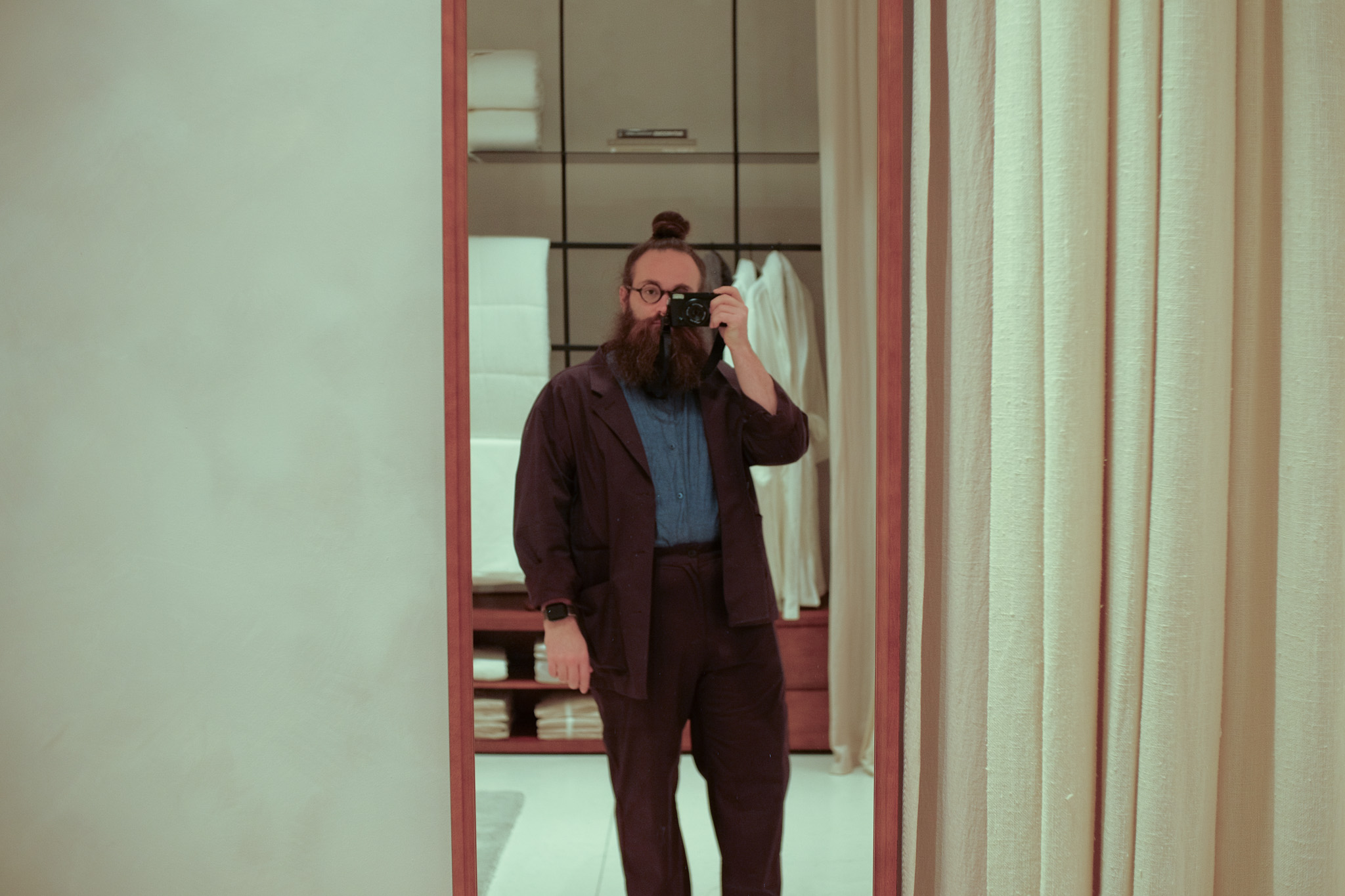 A man with a bun wearing a purple suit in a room taking a picture in a mirror