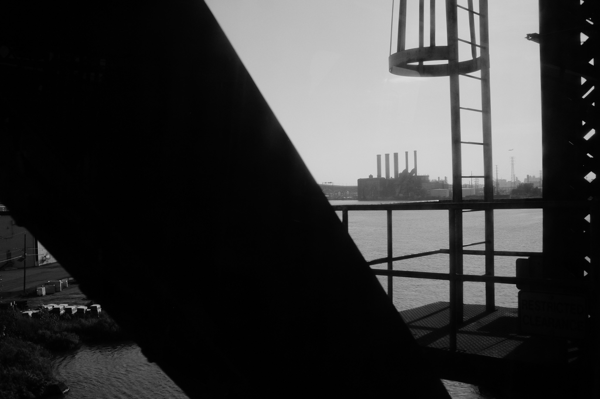 A factory on the river as seen through a metal truss bridge.