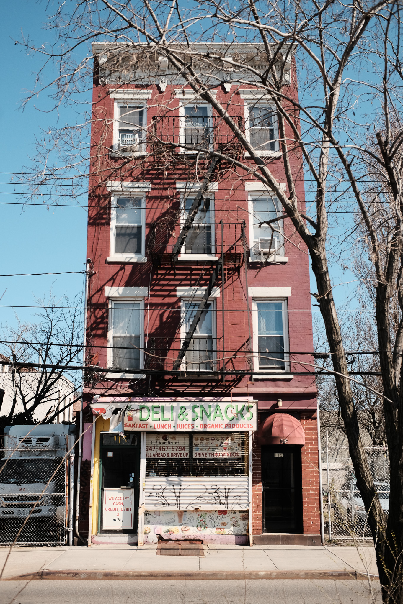 A closed deli in a thin red building surrounded by now empty lots.