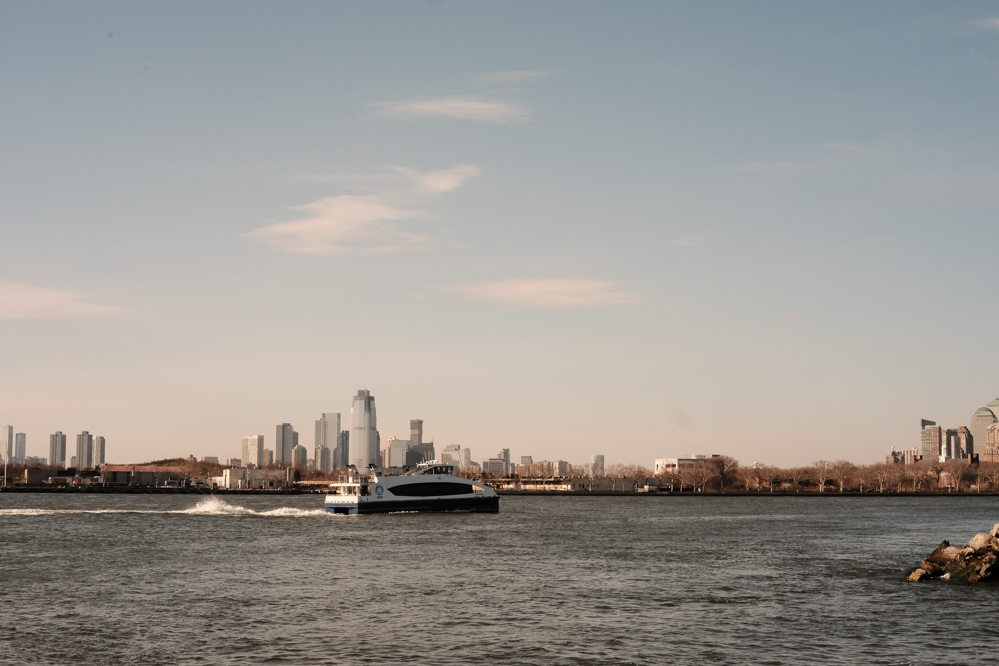 The NY Ferry speeding along in the bay with Jersey City in the distance.