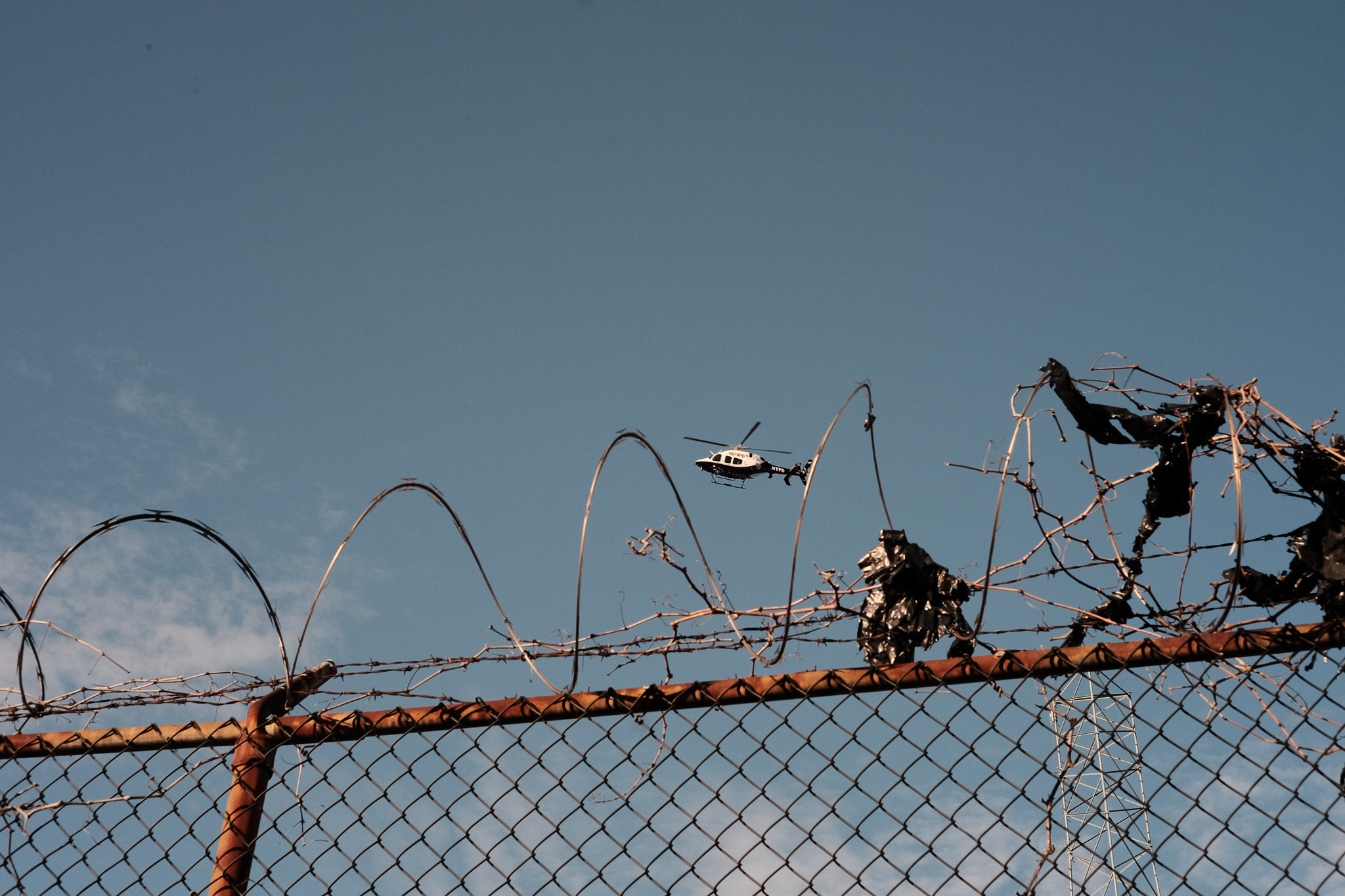 A police helicopter hovers low over a chain link fence topped with barb wire